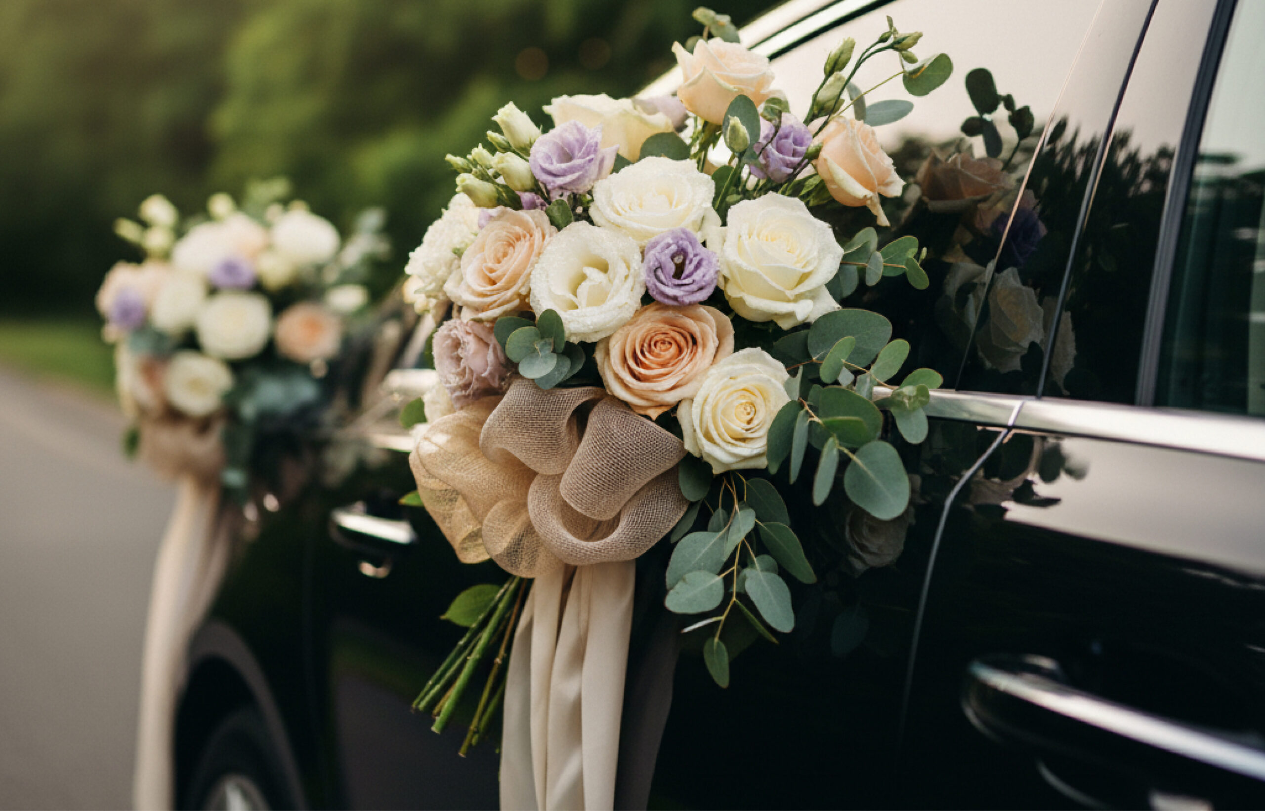 Wedding bouquet of cream and blush roses with eucalyptus tied to a black car door.
